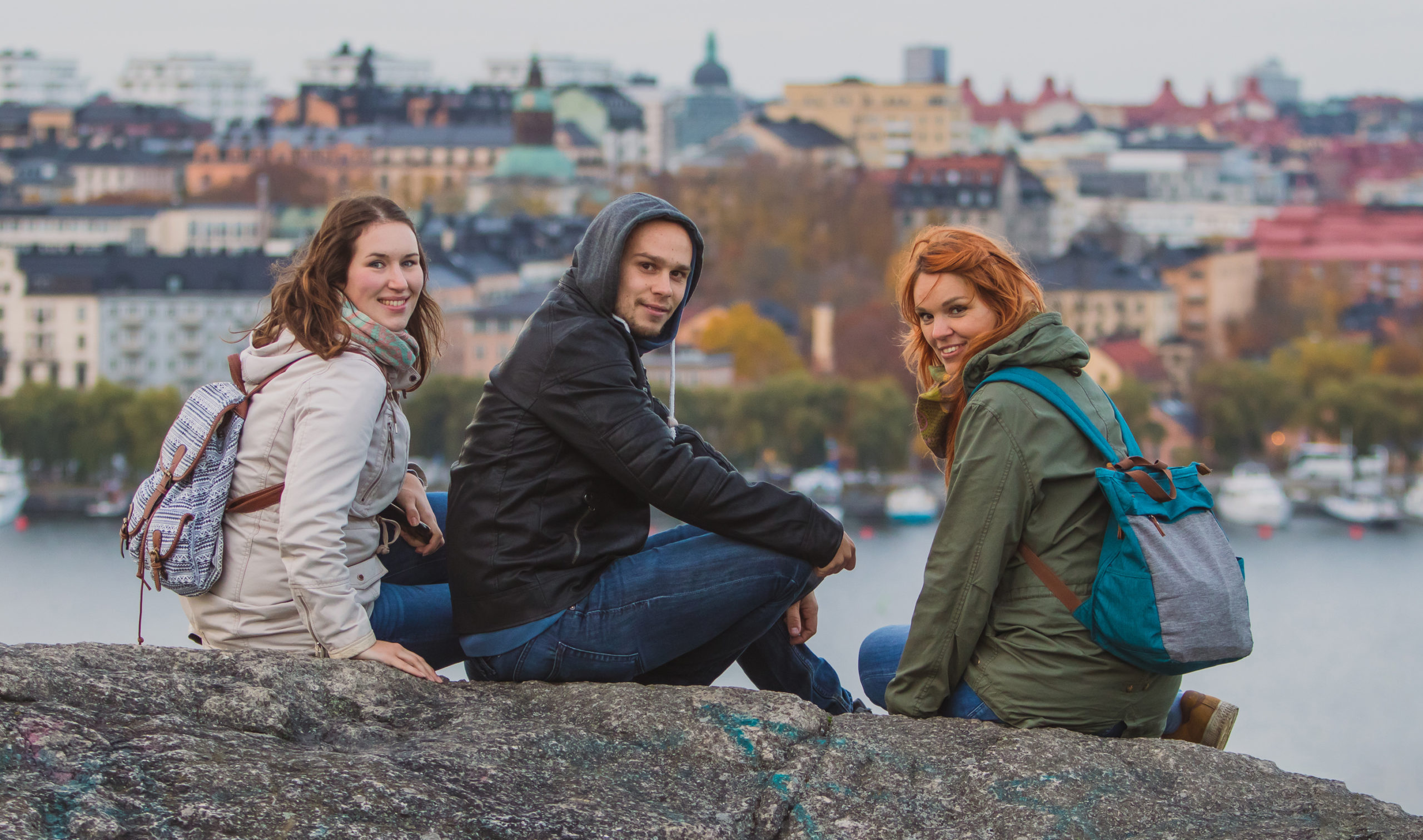 Three people sitting on a rock behind them there is a city